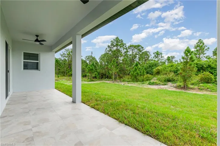 View of green lawn with ceiling fan, a patio area, and view of wooded area