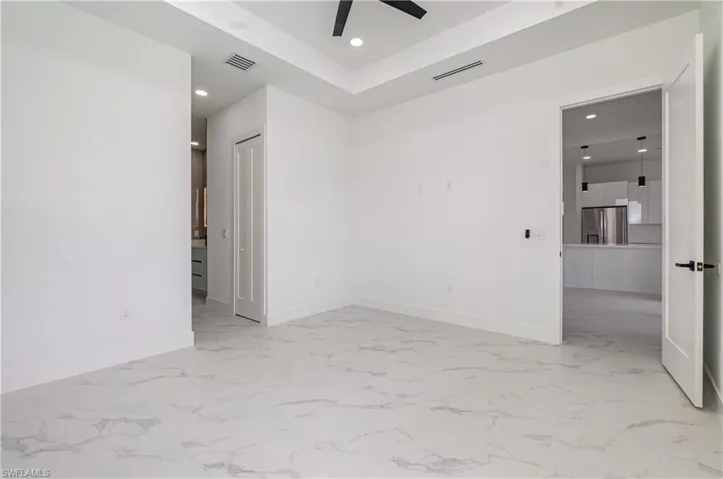 Spare room with recessed lighting, light marble finish floors, a tray ceiling, and a ceiling fan
