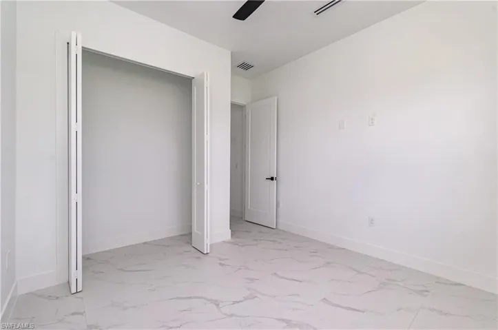 Unfurnished bedroom featuring light marble finish flooring, ceiling fan, and a closet