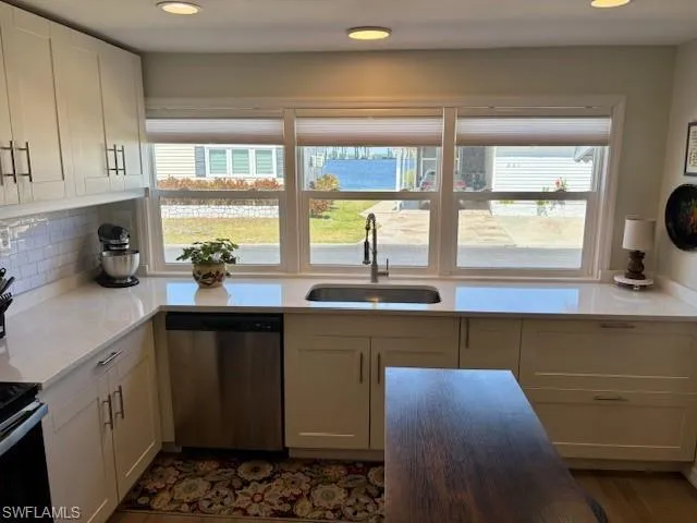 Kitchen featuring white cabinets, stainless steel dishwasher, a sink, decorative backsplash, and light countertops