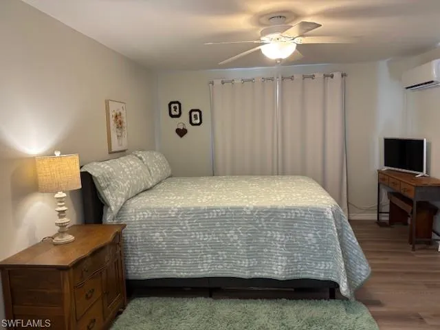 Bedroom with wood finished floors, an AC wall unit, and ceiling fan