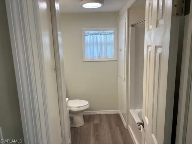 Full bath with washtub / shower combination, wood finished floors, toilet, and baseboards