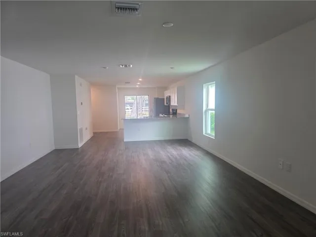 Unfurnished living room featuring baseboards and dark wood-style flooring