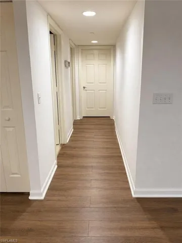 Hallway featuring wood-finish flooring, recessed lighting, white trim, and light-colored paneled doors