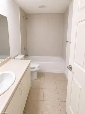 Bathroom featuring a shower-tub combination with light-toned subway tile surround, a white vanity with integrated sink, and square tile flooring