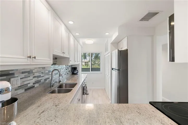 Kitchen featuring white cabinets, light stone counters, recessed lighting, freestanding refrigerator, and decorative backsplash