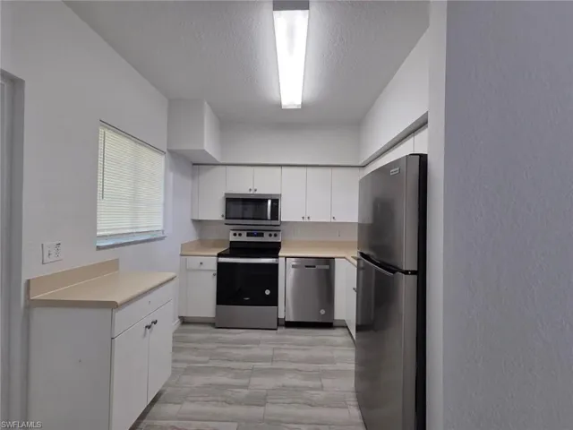 Kitchen with stainless steel appliances, light countertops, white cabinets, a textured wall, and a textured ceiling