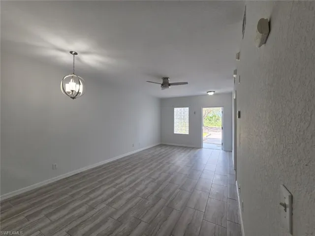 Unfurnished room with wood finish floors, a ceiling fan, a chandelier, and a smoke detector