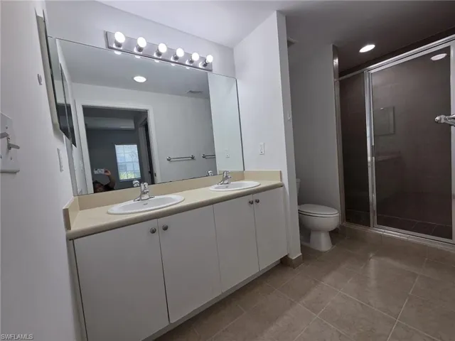 Ensuite bathroom with double vanity, a stall shower, and light tile patterned floors