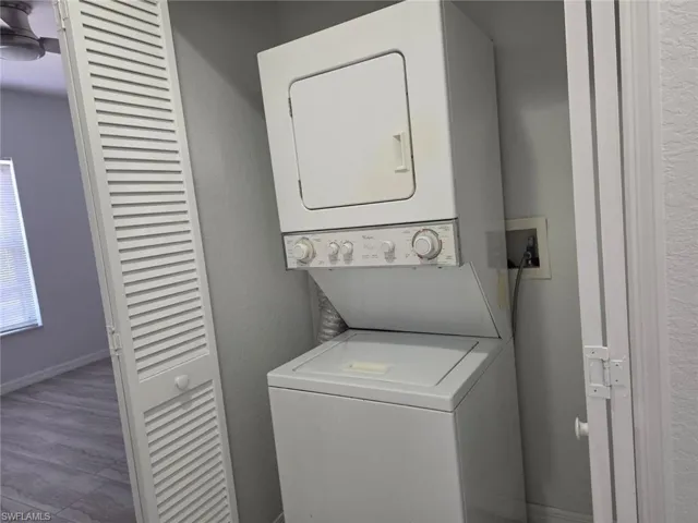Laundry area featuring a textured wall, stacked washer and dryer, and light wood finished floors