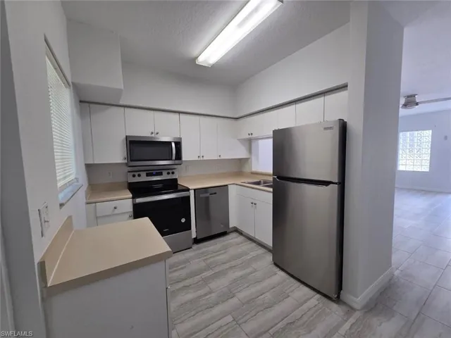 Kitchen featuring stainless steel appliances, light countertops, white cabinets, and a textured ceiling