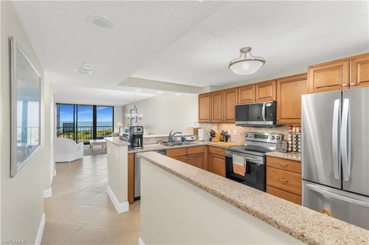Kitchen with stainless steel appliances, a peninsula, wood finish cabinetry, light tile patterned flooring, and hanging light fixtures