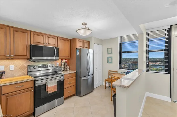 Kitchen with stainless steel appliances, wood finish cabinets, light stone counters, a textured ceiling, and light tile patterned floors