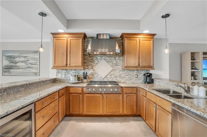 Kitchen with decorative light fixtures, wine cooler, wall chimney exhaust hood, sink, and light tile floors