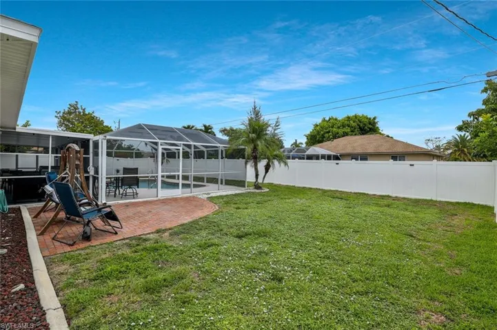 Expansive backyard featuring a screened-in pool enclosure, red brick paver patio, established palm trees, and a white privacy fence