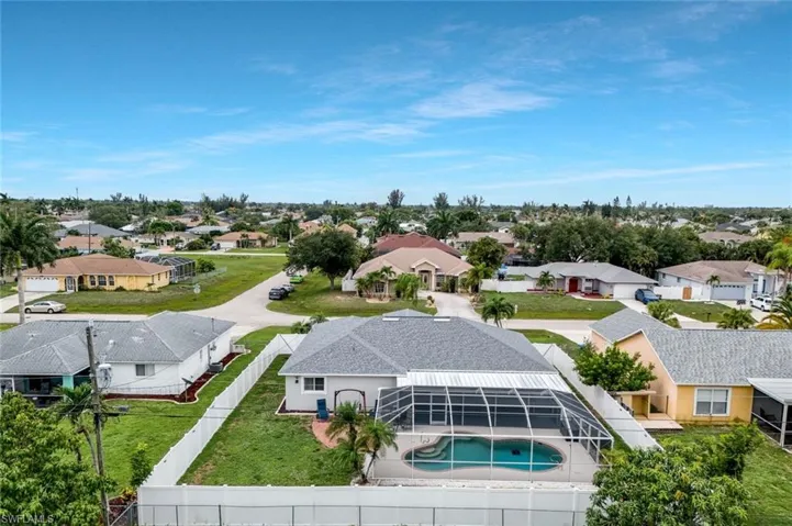 Rear exterior featuring a screened pool enclosure, paved pool deck, and a white privacy fence