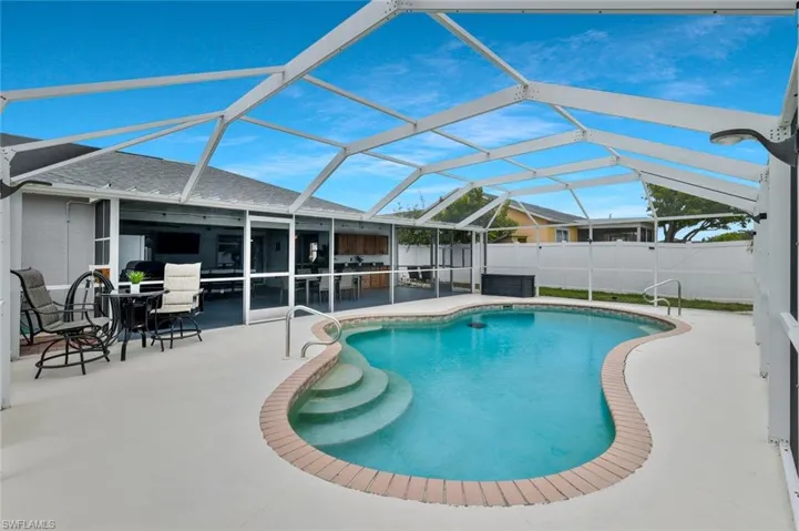 Screened-in outdoor pool area featuring a freeform swimming pool with brick coping, integrated steps, and a spacious concrete deck