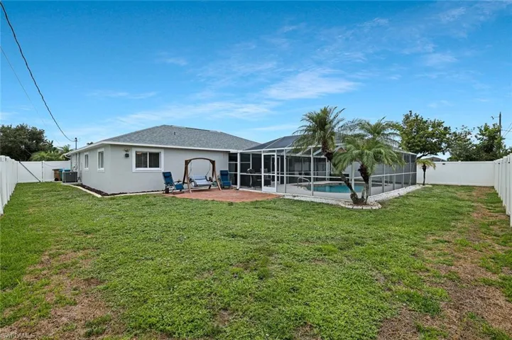 Expansive backyard featuring a screened-in pool enclosure, mature palm trees, a white perimeter fence, and a dedicated patio area