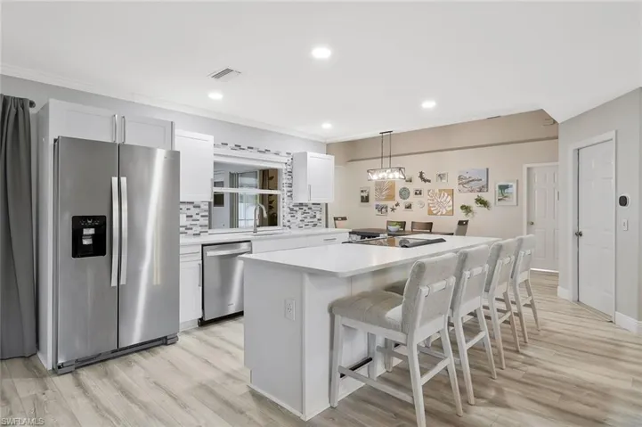 Open-concept kitchen featuring an oversized island with seating, stainless steel appliances, light wood-finish flooring, white cabinetry, and recessed lighting