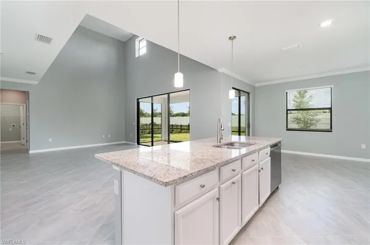 Kitchen with light stone counters, hanging light fixtures, white cabinetry, open floor plan, and an island with sink