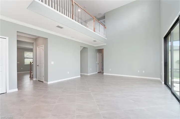Unfurnished living room featuring a high ceiling, light tile patterned floors, and crown molding