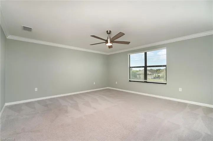 Empty room with ornamental molding, light carpet, and a ceiling fan