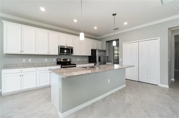 Kitchen with ornamental molding, light stone countertops, appliances with stainless steel finishes, white cabinetry, and a center island with sink