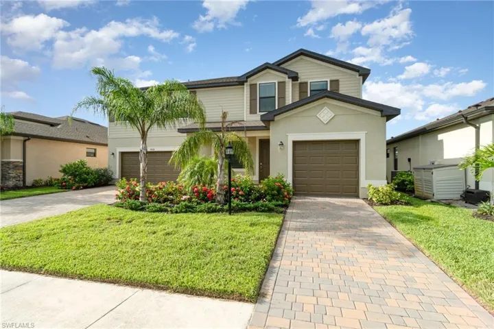 Traditional-style home featuring decorative driveway, stucco siding, a front lawn, and a garage