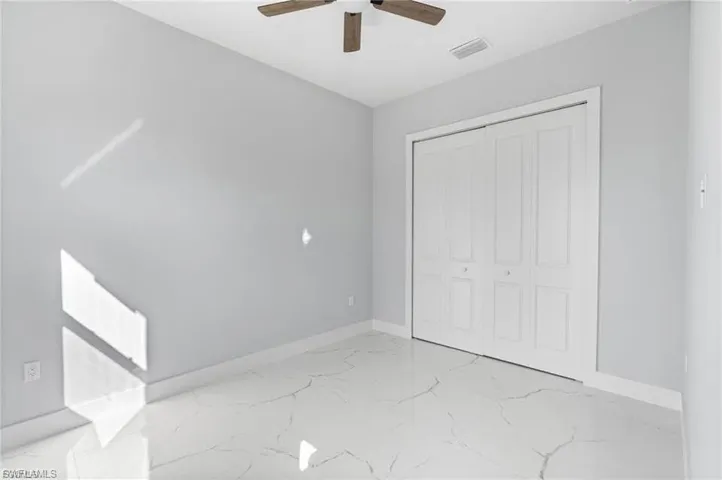 Neutral-toned room featuring a wood-finish ceiling fan, white bi-fold closet doors, and large-format white tile flooring with veining