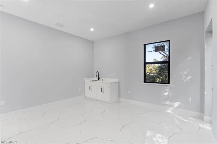 Spacious room featuring white large-format tile flooring, a built-in wet bar with a white cabinet and black faucet, and a black-framed window