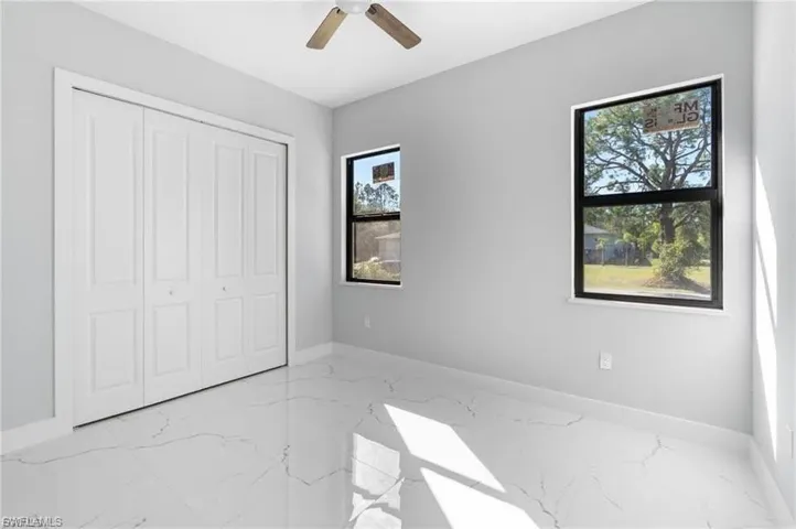 Spacious room featuring large windows, a ceiling fan, bifold closet doors, and marble-look tile flooring