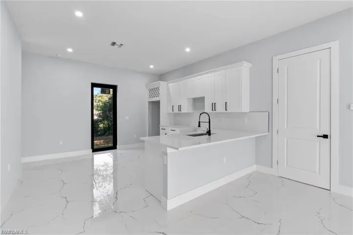 Modern kitchen featuring a white island with an integrated sink and matte black faucet, white shaker cabinetry with matte black hardware, and an adjacent pantry door