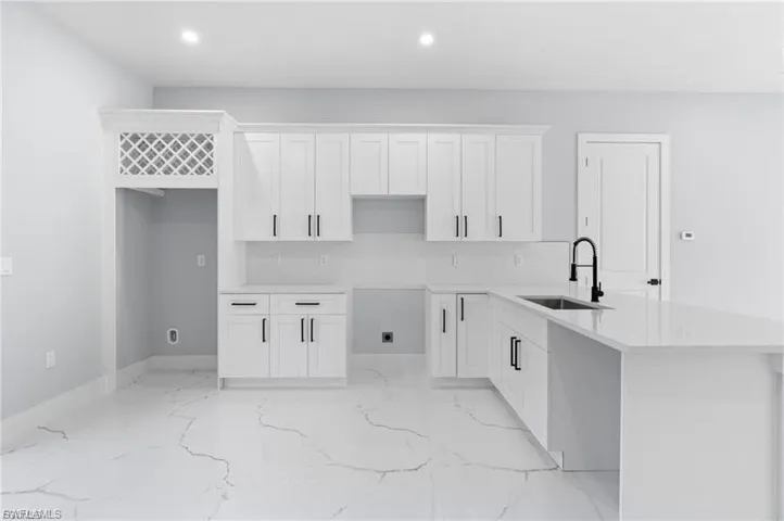 Contemporary kitchen featuring white shaker cabinetry, quartz countertops, a matte black faucet, and large format tile flooring with distinctive veining