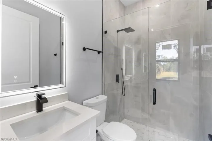 Modern bathroom featuring a frameless glass shower enclosure with matte black fixtures, a rain shower head, and a handheld spray