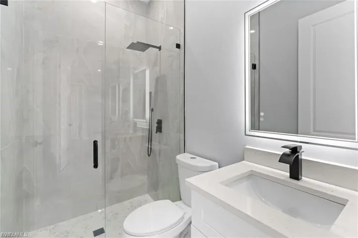 Modern bathroom featuring a glass-enclosed shower with large format tile, a rain shower head, and matte black fixtures