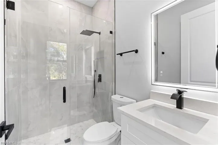 Contemporary bathroom featuring a frameless glass shower enclosure with a rainfall showerhead, large format tiled walls, and a white vanity with an integrated sink, quartz-finish countertop, and matte black faucet