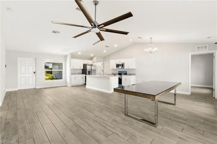 Unfurnished living room featuring vaulted ceiling, ceiling fan, wood finish floors, and a chandelier