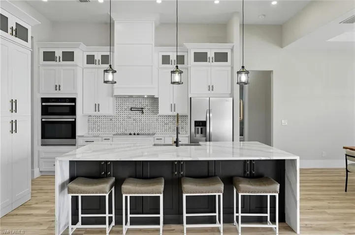 Kitchen with light stone countertops, decorative backsplash, white cabinetry, a breakfast bar, and recessed lighting
