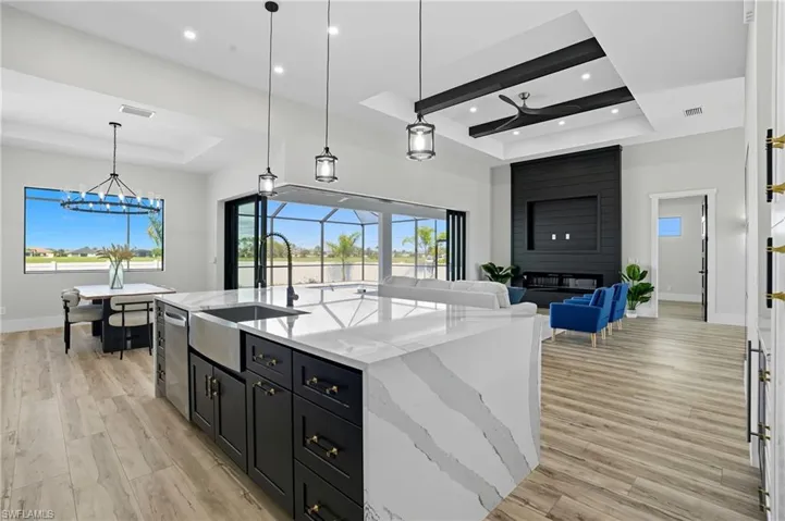 Kitchen with a raised ceiling, decorative light fixtures, light stone countertops, dark cabinetry, and recessed lighting