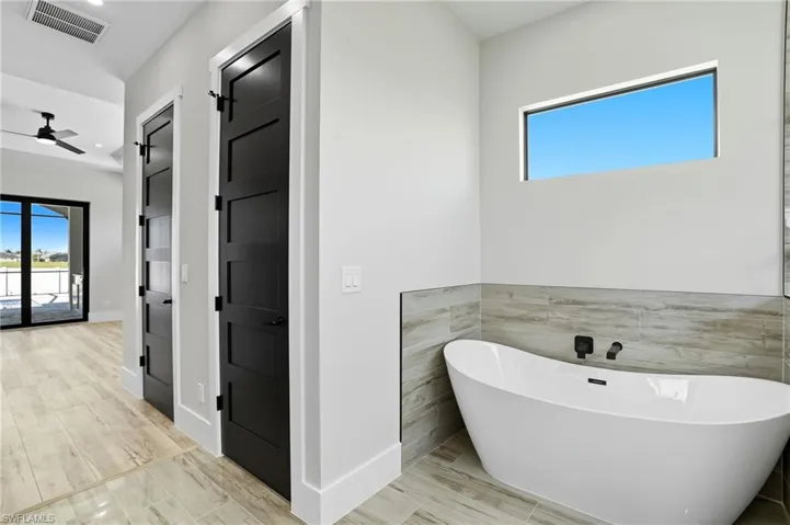 Bathroom with a freestanding bath, wood finish floors, tile walls, and a ceiling fan