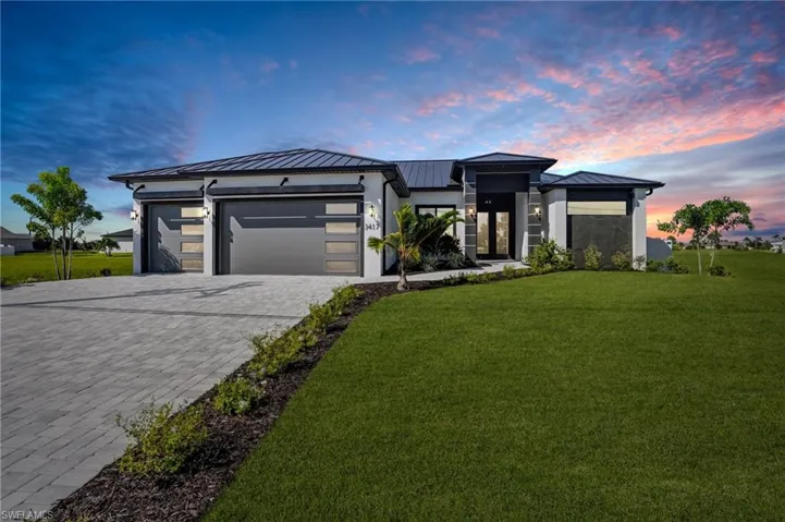 View of front of house with a standing seam roof, a metal roof, an attached garage, decorative driveway, and a yard