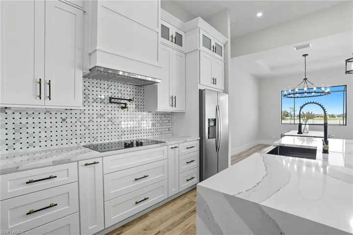 Kitchen featuring light stone counters, light wood finished floors, decorative light fixtures, and white cabinetry