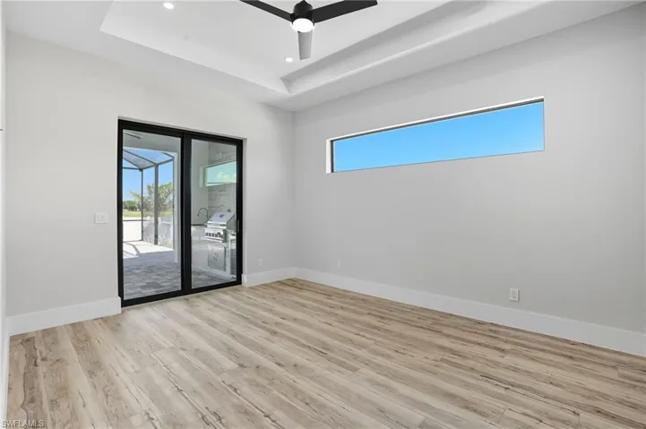 Spare room with healthy amount of natural light, light wood finished floors, a tray ceiling, a ceiling fan, and recessed lighting