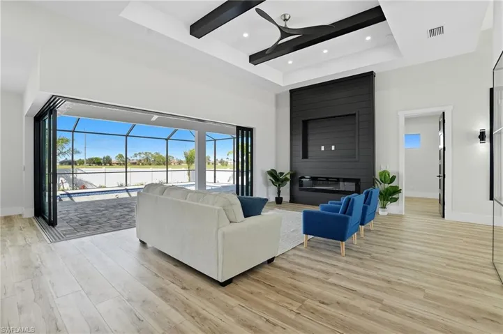 Living room with plenty of natural light, a sunroom, light wood-style flooring, a towering ceiling, and beamed ceiling