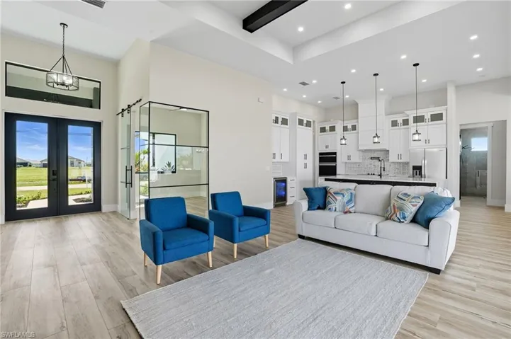 Living room featuring plenty of natural light, light wood-type flooring, a high ceiling, french doors, and recessed lighting