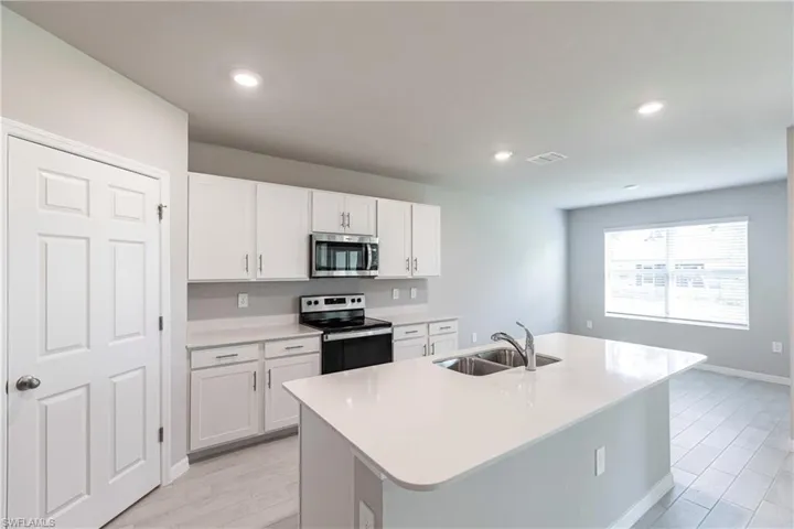 Kitchen with stainless steel appliances, light hardwood / wood-style floors, white cabinetry, sink, and a kitchen island with sink