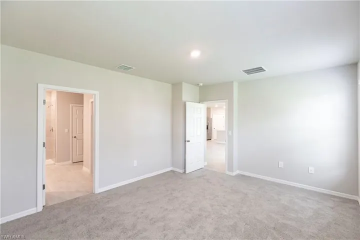 Unfurnished bedroom featuring ensuite bathroom and light colored carpet