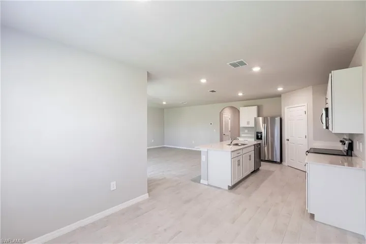 Kitchen with light wood-type flooring, appliances with stainless steel finishes, white cabinetry, sink, and a center island with sink
