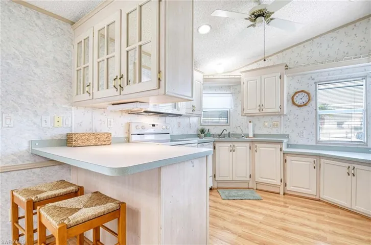 Kitchen featuring white appliances, white cabinets, a textured ceiling, kitchen peninsula, and a breakfast bar area