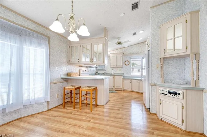 Kitchen featuring a kitchen bar, light wood-type flooring, a textured ceiling, white refrigerator, and hanging light fixtures